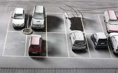 Photograph of light snow on cars in a parking lot in Formello, Italy. The view-angle is looking down from a considerable height above. Tracks of a recently departed car are evident, as is the wind direction during the snow-fall.