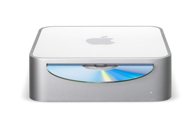 A photograph showing the Mac mini personal computer against a white background. The Mac mini's design is minimal, with only a CD slot and status light on the front.