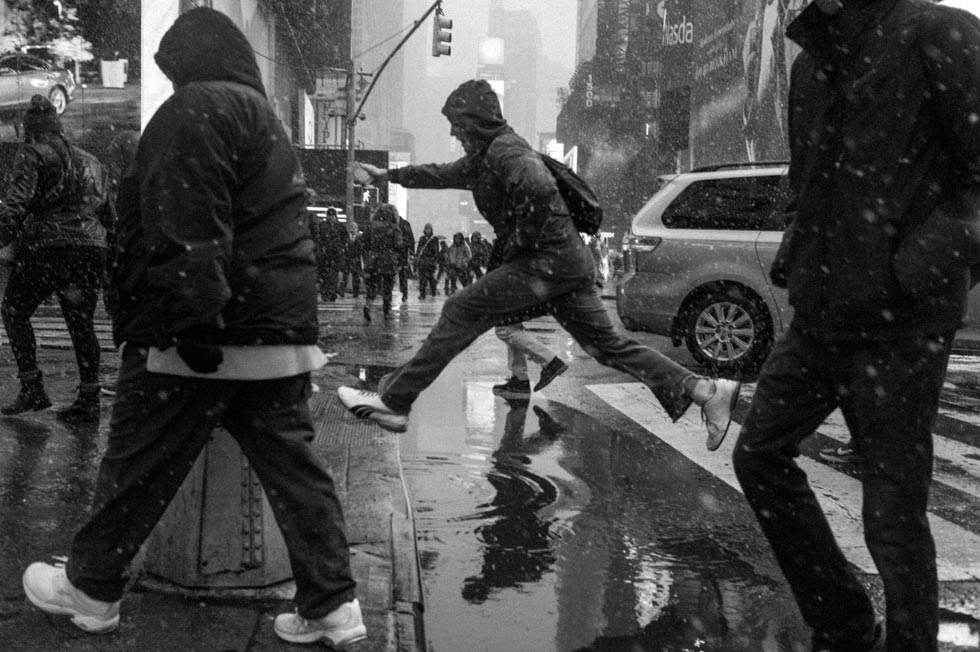 Street photograph of a figure jumping over a puddle on 42nd Street near Times Square, NYC.